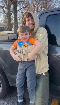 a man holding a young boy in front of a truck