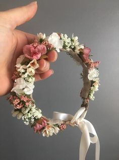 a hand is holding a flower wreath with white and pink flowers on the inside of it