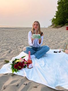 a woman sitting on the beach holding a cake with candles in her hands and flowers