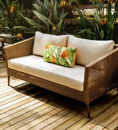 a couch sitting on top of a wooden floor next to green plants and flowers in the background