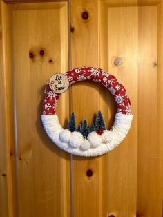 a christmas wreath hanging on a wooden door with pine trees and snowflakes around it