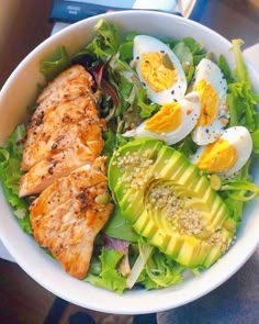 a white bowl filled with chicken, avocado and hard boiled eggs on top of lettuce