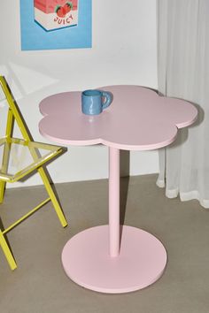 a pink table with a cup on it next to a yellow chair and a painting