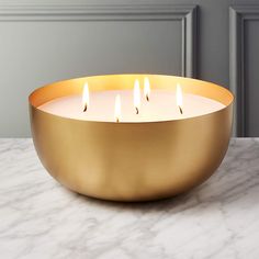 a gold bowl filled with lit candles on top of a marble countertop next to a gray wall