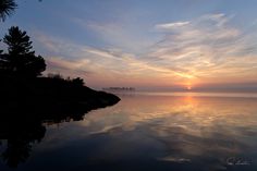 the sun is setting over water with trees in the foreground and clouds in the background