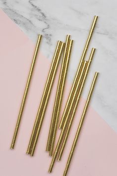 four gold straws sitting on top of a pink and white table next to each other