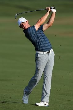 a man swinging a golf club on top of a green field