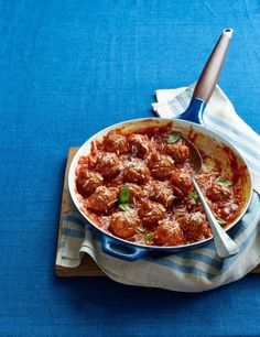 meatballs and tomato sauce in a pan on a blue tablecloth with a spoon