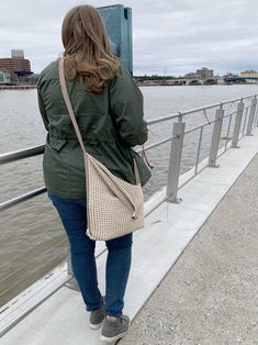 a woman standing on the edge of a bridge looking at the water and buildings in the distance