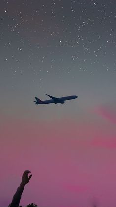 an airplane flying in the night sky with stars above it and a person holding their hand up