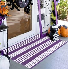 halloween decorations on the front porch with purple and white striped rug, pumpkins and spider web