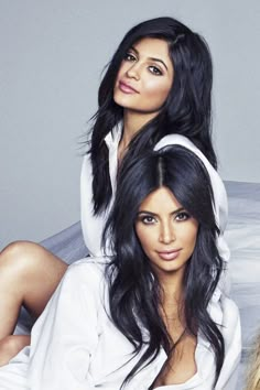 two beautiful women sitting on top of a bed next to each other in white shirts