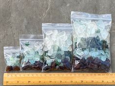 three bags of sea glass sitting next to a ruler