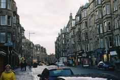 a woman walking down the street in front of some tall buildings with cars parked on both sides