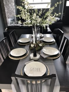 a dining room table set with plates and flowers in a vase on the centerpiece