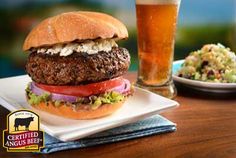 a hamburger with lettuce, tomato and onion next to a glass of beer