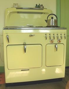 an old fashioned yellow stove with a pot on it's burner and oven door