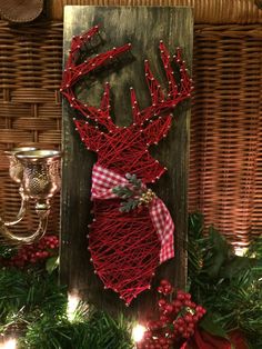 a red string deer head hanging on a wooden plaque surrounded by greenery and candles