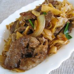 a white plate topped with meat and noodles on top of a tablecloth covered table