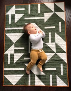 a baby laying on top of a green and white quilt