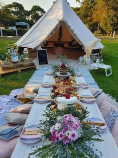 a table set up with plates and flowers on it in front of a teepee tent