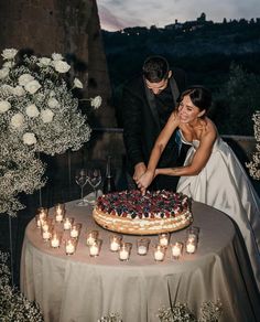 a bride and groom are cutting their wedding cake at the table with candles in front of them