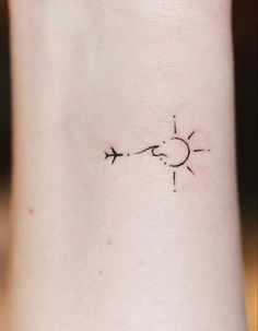 an arrow and sun tattoo on the left side of the wrist is shown in black ink