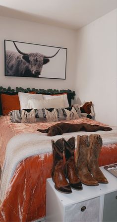 there is a bed with cowboy boots on it and a cow painting above the bed