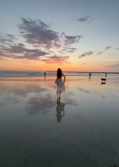 a woman is walking on the beach at sunset with her dog and three other people in the background