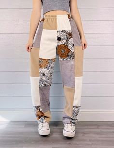 a woman standing in front of a white wall wearing pants with flowers on the side