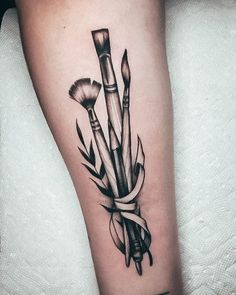 a black and white photo of a tattoo with brushes on the arm that is wrapped in ribbon