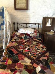 a bed with a quilt on top of it next to a night stand and dresser