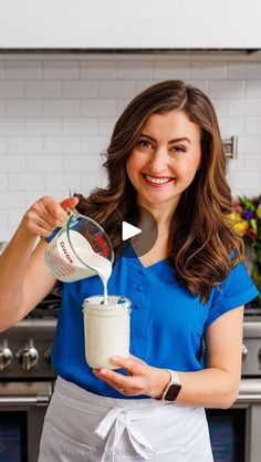 a woman in an apron is pouring something into a jar with a ladle on it