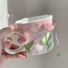 a hand holding a coffee mug with pink roses on it and green leaves flying around