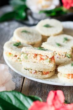 several small sandwiches on a plate with flowers in the background