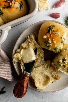 a white plate topped with rolls covered in butter and herbs next to a bowl of dip