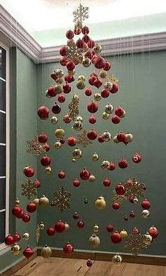 a christmas tree made out of red and gold ornaments hanging from the ceiling in an empty room