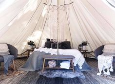 a bed sitting inside of a white tent next to two chairs and a table in front of it