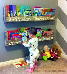 a baby standing in front of two bookshelves with stuffed animals on the floor