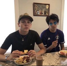 two young men sitting at a table with plates of food and drinks in front of them