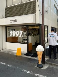 an ice cream cone is in front of a store on the side of the street