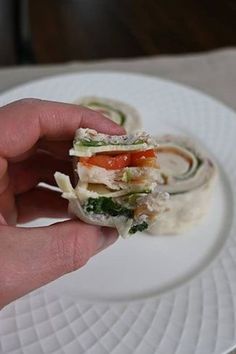 a hand holding a small sandwich on top of a white plate