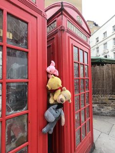 two stuffed animals are sitting in the doorway of a phone booth with red telephone booths