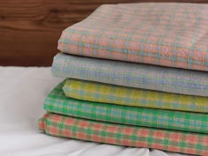 four different colored plaid sheets stacked on top of each other in front of a wooden headboard