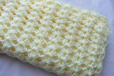 a crocheted yellow and white blanket laying on top of a bed next to a pillow