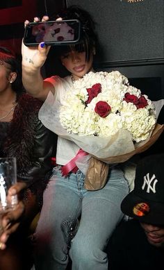 a woman taking a photo with her cell phone while holding a bouquet of white and red flowers