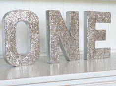 the word one is made out of silver glitters on a white shelf in front of a brick wall