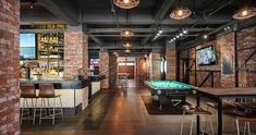 an indoor bar with pool tables and stools in front of brick walls, along with lots of lights