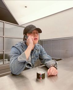 a person sitting at a table with a cell phone to their ear and a can of soda in front of them