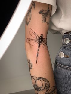 a woman's arm with a dragon tattoo on it and flowers in the background